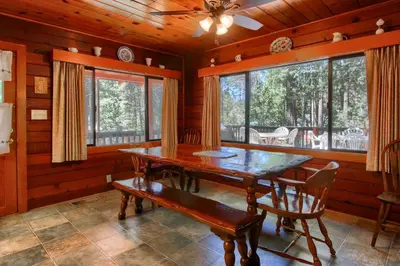 a dining room with a wooden table and chairs and windows at Deer Creek in Wawona