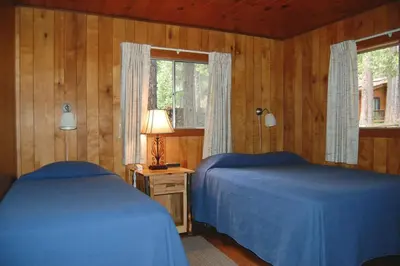 two beds in a bedroom with wooden walls and a window at Harmony Villa in Wawona