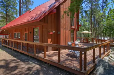 a cabin with a large deck in the woods at Jolie Cabin in Wawona