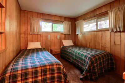 two beds in a room with wooden walls and windows at Yosemite Mountain Lodge in Wawona