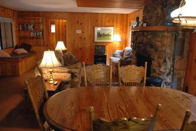 a living room with a table and a stone fireplace at Burke's Place in Wawona