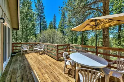 a deck with a table and chairs and an umbrella at Bear Haus - Sledding At Cabin - Forest Views - Foosball in South Lake Tahoe