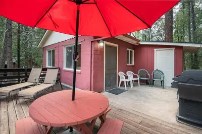 a red table and chairs on a deck with a house at Yosemite's Riverfront Retreat in Wawona