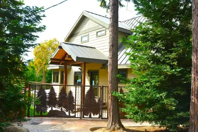 a yellow house with a gate and trees at Deer Lodge #1 Lake front in Bass Lake