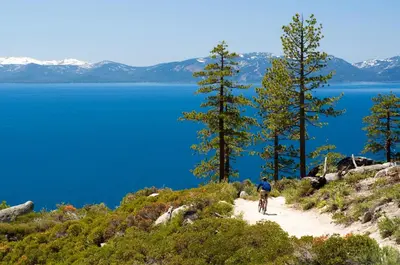 a man riding a bike on a dirt trail next to a lake at Mountain Getaway - Lake Tahoe - Incline Village - Private Garage in Incline Village