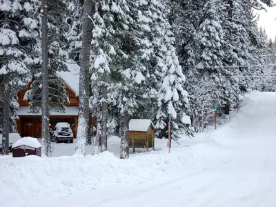 a house covered in snow in front of trees at Traditional Log Cabin Rental for Couples on the West Shore of Lake Tahoe, California in Tahoe City