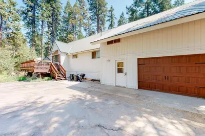 a white barn with a garage and a driveway at CC Cabin - Full Game Room & Wrap Around Deck in Shaver Lake