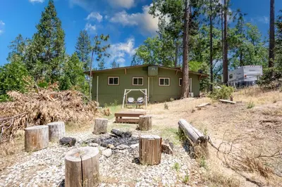 a green building with a fire pit in front of it at Immersed in Nature Manzanita Cabin with Hot Tub in Oakhurst