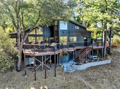 a house with a large deck and a tree at Spacious Mountain View Home - Pool, Spa & Game Rm in Oakhurst