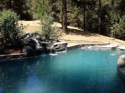a pool of blue water with a waterfall at Gorgeous Vacation Rental with Hot Tub near Yosemite National Park, California in Mariposa