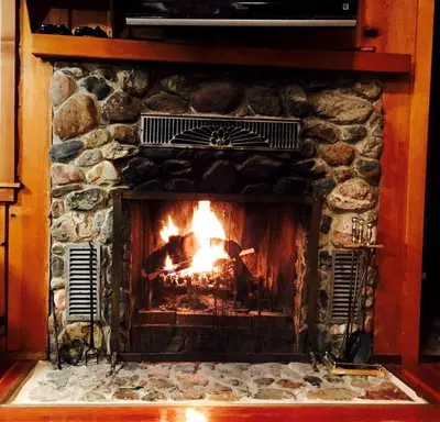 a stone fireplace with a fire in it at Cozy Riverside Cabin Rental with Easy Access to Chilnualna Falls in California in Wawona