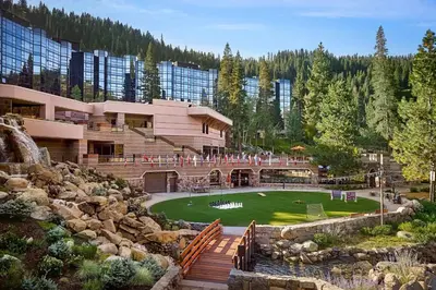 a building with a green yard in front of a mountain at Everline Resort & Spa Palisades- Forest View in Olympic Valley