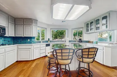 a kitchen with white cabinets and two bar chairs at Deer Paradise in Coarsegold