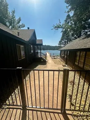 a house with a fence next to a lake at Lewis Cabin - Boat Dock - Lake Front - Sleeps 10 in Bass Lake