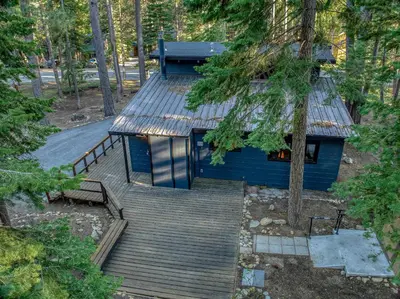 a blue house with a wooden deck in the woods at Laid-Back Tahoe Stay Walk to Lake & EV Charger in Homewood