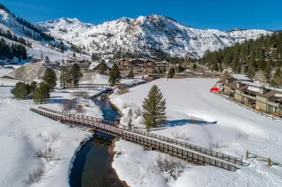 a bridge over a river with snow covered mountains at Serene Condo by Palisades Base and Golf Course in Olympic Valley
