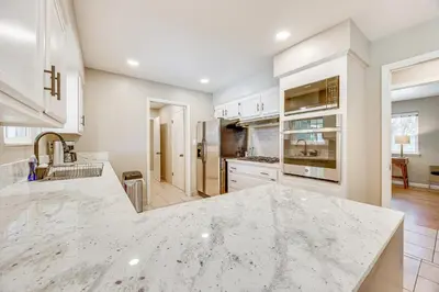 a kitchen with white cabinets and a marble counter top at Shop, Hike and Explore Fresno Home with Private Pool! in Fresno