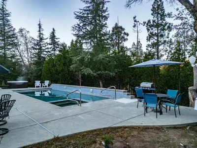 a swimming pool with chairs and a table and an umbrella at Scenic Mountain Views w Heated Pool, Game Room, and Hottubs in Oakhurst
