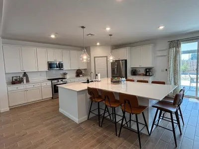 a kitchen with white cabinets and a large island with bar stools at Joyhouse in Visalia