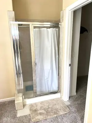 a glass shower door with a white shower curtain at la paz private room with jacuzi in Fresno