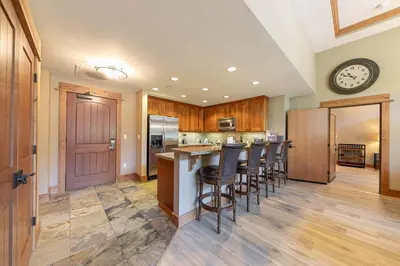 a kitchen with a bar with chairs and a clock on the wall at Catamount Lodge 101 by East West Hospitality in Truckee