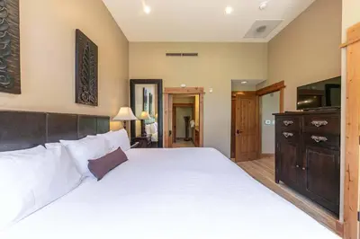 a bedroom with a large white bed with a wooden headboard at Catamount Lodge 101B by East West Hospitality in Truckee