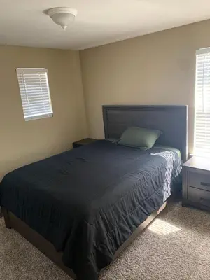 a bedroom with a bed with a blue bedspread and two windows at Furnished five bedroom and gated community in Patterson