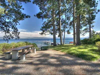 a picnic bench sitting on the grass near the water at Hoeck Hacienda By Hauserman Rentals in Tahoe City