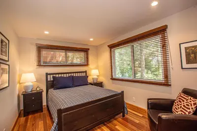 a bedroom with a bed and a chair and two windows at Coates By Hauserman Rentals in Tahoe City