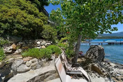a bench sitting next to a tree next to a body of water at Rygh Lakefront By Hauserman Rentals in Carnelian Bay