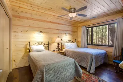 two beds in a log cabin bedroom with a ceiling fan at 42A Megan in North Wawona
