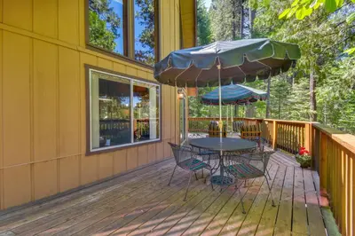 a table and chairs on a deck with an umbrella at Walk to Fly-In Lake Blue Lake Springs Cabin! in Arnold