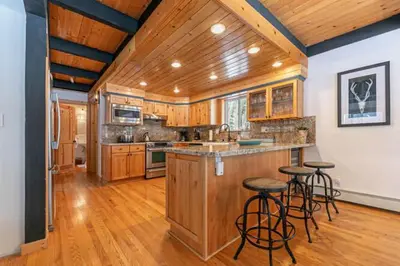 a large kitchen with wooden cabinets and bar stools at Lakewalk Lodge at the West Shore by Tahoe Getaways, Pet-Friendly w Sauna! in Homewood