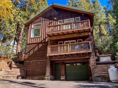 a log cabin with a balcony and a garage at Enchanting Creekside Cabin Retreat near Yosemite National Park in California in Oakhurst