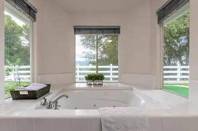 a large white bath tub in a bathroom with two windows at Yosemite and Bass lake I Hot tub I Game room I Sleeps 13 in Oakhurst