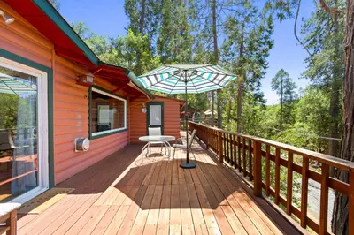 a wooden deck with a table and an umbrella at Red Cabin in Twain Harte - King bed in Twain Harte
