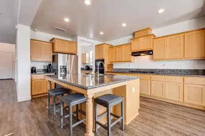 a kitchen with wooden cabinets and a island with bar stools at 1 Mi to Golf! Spacious and Modern Home in Dinuba in Dinuba