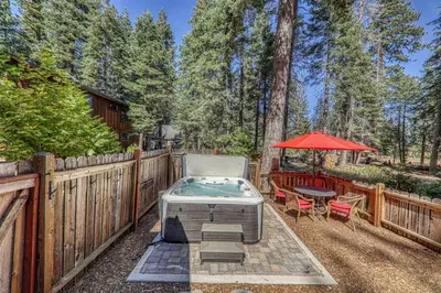 a backyard with a hot tub and a table and umbrella at Classic Cabin in the Pines by Tahoe Getaways - Walk to Lake, Pet-Friendly 3 BR w Yard & Hot Tub! in Homewood
