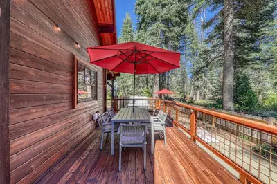 a wooden deck with a table with chairs and an umbrella at Classic Cabin in the Pines by Tahoe Getaways - Walk to Lake, Pet-Friendly 3 BR w Yard & Hot Tub! in Homewood