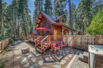 a cabin in the woods with red chairs and a fence at Classic Cabin in the Pines by Tahoe Getaways - Walk to Lake, Pet-Friendly 3 BR w Yard & Hot Tub! in Homewood