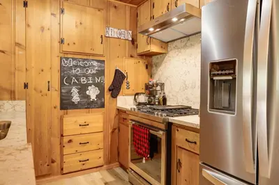a kitchen with wooden cabinets and a stainless steel refrigerator at Community Lake Access Peaceful Cabin in Sonora! in Sonora