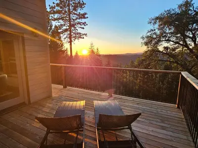 a deck with two chairs and a table and the sunset at Cedar Rock Cabin in Mi-Wuk Village