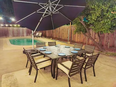 a wooden table with chairs and an umbrella next to a pool at Old Fig House - Historic Fig Garden Neighborhood in Fresno