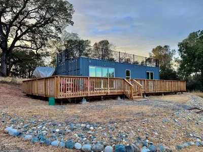 a blue house with a deck on a field at Unique Container, Home 20 Acres, Modern Stay in Placerville