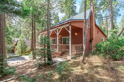 a small red cabin in the woods with a porch at Dogwood Star Star Location Cozy Vibes in Shaver Lake