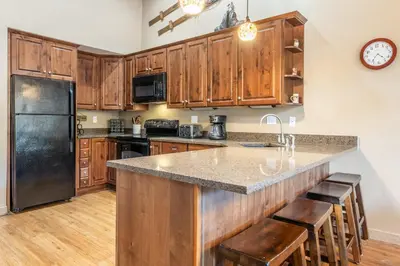 a kitchen with wooden cabinets and a large island with bar stools at Updated1849 Townhome #611, Steps to Canyon Lodge 4 Bed/3BA, hot tubs, game rm, sauna! in Mammoth Lakes