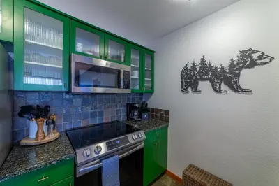 a kitchen with green cabinets and a bear decal on the wall at Posh Village 2/2; Ski-In/Out + Premiere Perks! in Mammoth Lakes