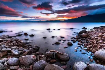a sunset over the water with rocks on the shore at Modern Rustic Lux Tahoe Cabin in Carnelian Bay