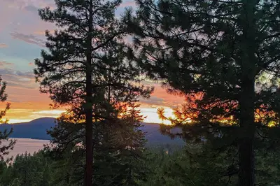 a sunset behind two trees in front of a lake at Dog-Friendly Retreat with Lake Views in Kings Beach in Kings Beach