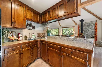 a kitchen with wooden cabinets and a stone wall at Tranquil Treehouse near Fly-In Lake with Deck Dining & BBQ in Arnold